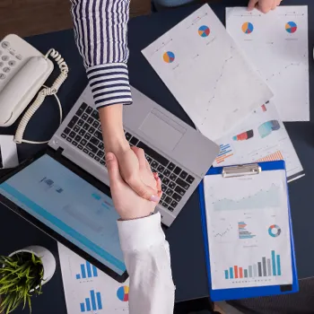 Shaking hands on table filled with important files