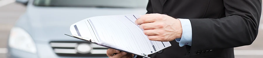 An image of a man holding paper works in front of a car