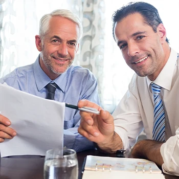 Two business people smiling in front of the camera while having a meeting and working together