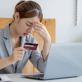 A woman holding bank card while touching her head as a sign of stress