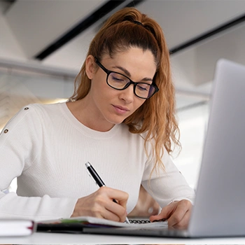 Woman in a ponytail and glasses writing on a paper