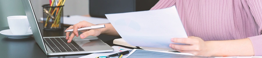 A person using a laptop while holding a paper