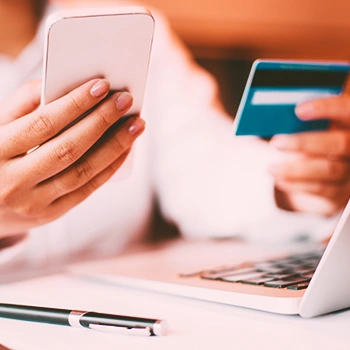 A woman holding his phone and credit card in front of his laptop