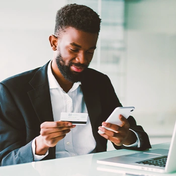 A man holding his phone and credit card in front of his laptop