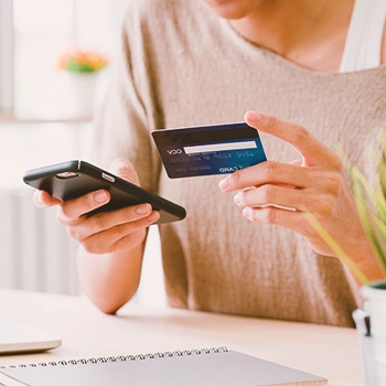 A woman holding his phone and credit card in front of his laptop