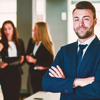 An office worker crossing arms facing the camera with colleagues at the background