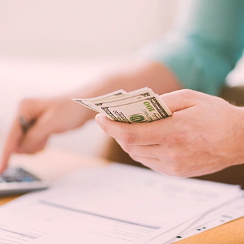 A person holding money while using a calculator