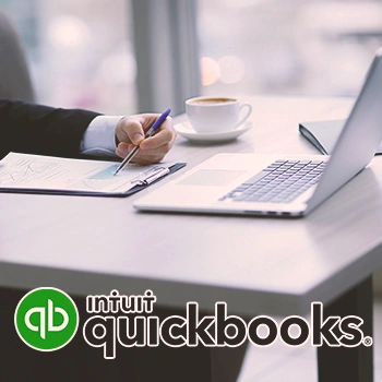 A person writing on paper while looking up what is QuickBooks all about