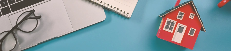 A miniature house beside a laptop on a blue table