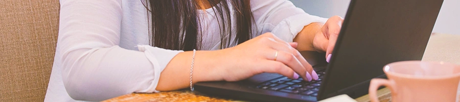 A woman using a laptop with a coffee mug on the side