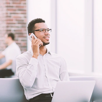 A person calling someone on the phone while using a laptop and looking up an llc in alabama