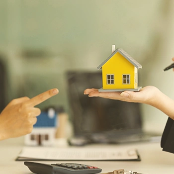 A person holding a miniature yellow house while another person points to it