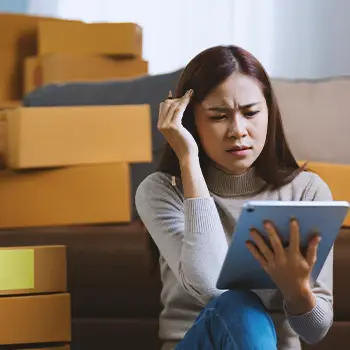 A person looking at a tablet while sitting on the floor beside stacks of boxes