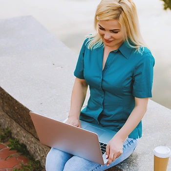 A person on her laptop outside with coffee beside her