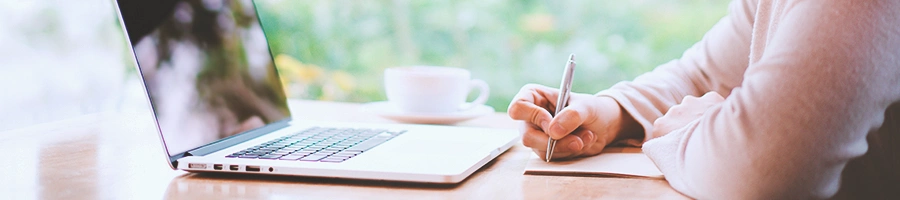 A person writing notes in front of a laptop