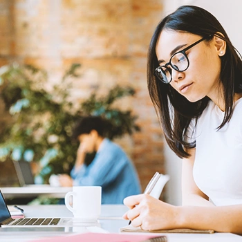 A businesswoman writing down notes in front of a laptop