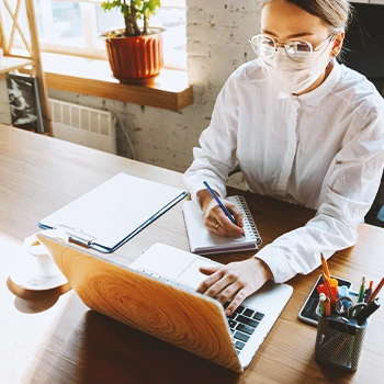 An office worker writing down on a notebook while working on a laptop