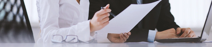 Two coworkers in front of a laptop while one holds a paper