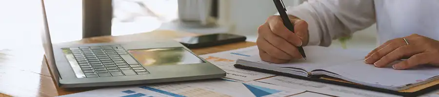 An office worker taking notes down in front of a laptop