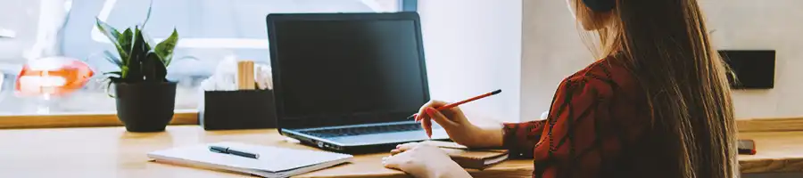 A person writing down notes in front of a laptop