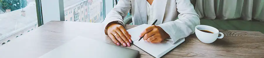 An office worker writing down on a notebook with coffee on the side