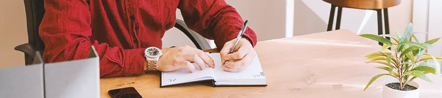 An office worker writing down notes in a notebook on a table