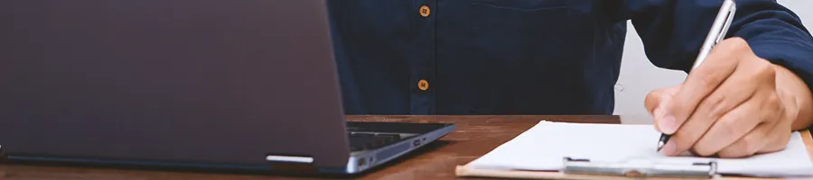 An office worker writing down notes while using the laptop