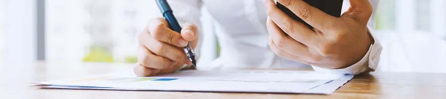 An office worker writing down things while looking at a phone