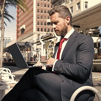 A business man searching for LLC name availability outdoors using a laptop