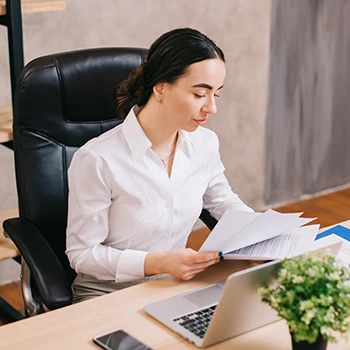 An image of a woman doing paper works while using a laptop