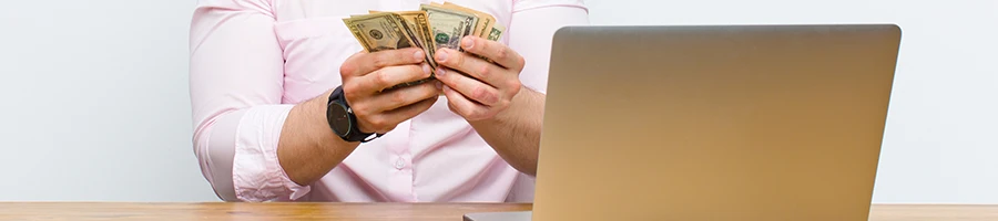 A business man counting money while using a laptop