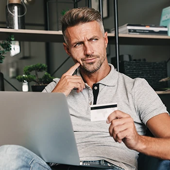 A man thinking while holding a credit card and using his laptop