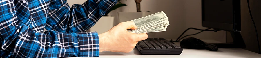 A man holding money in front of his computer