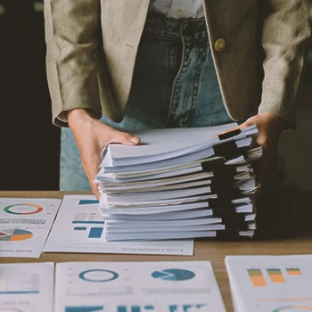 An office worker holding stacks of paperwork on a table