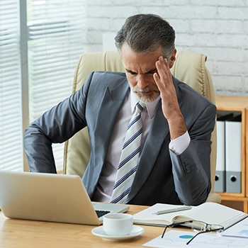 A businessman holding his forehead while looking at his laptop