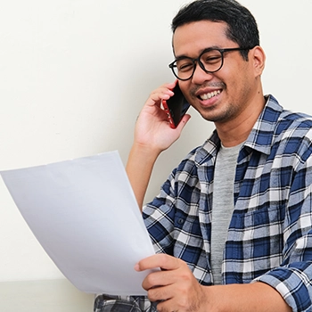 Smiling man holding a document while talking to phone